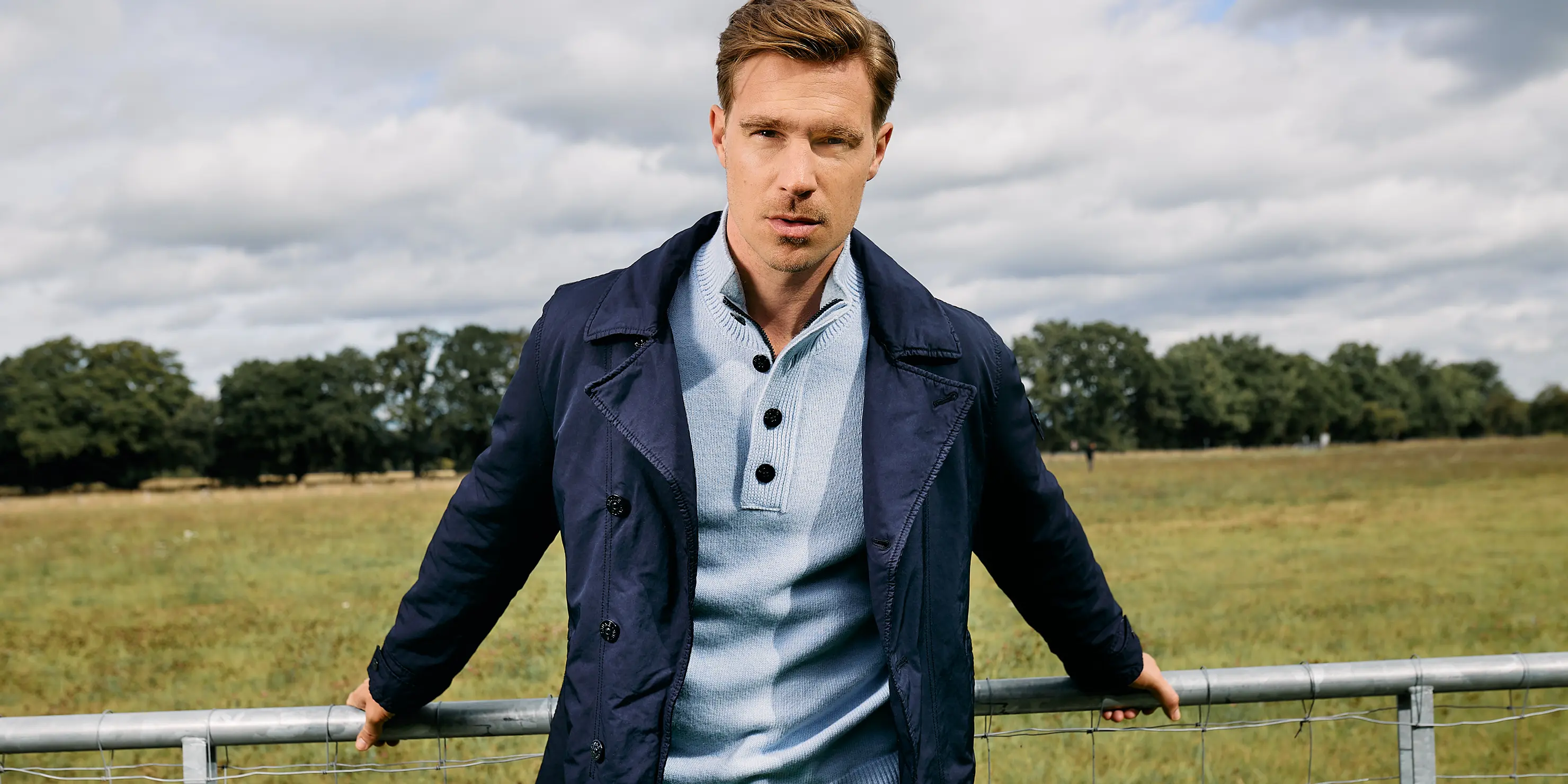 Das Bild zeigt einen Mann mit einem hellblauen Stone Island Pullover und dunkelblauen Stone Island Mantel