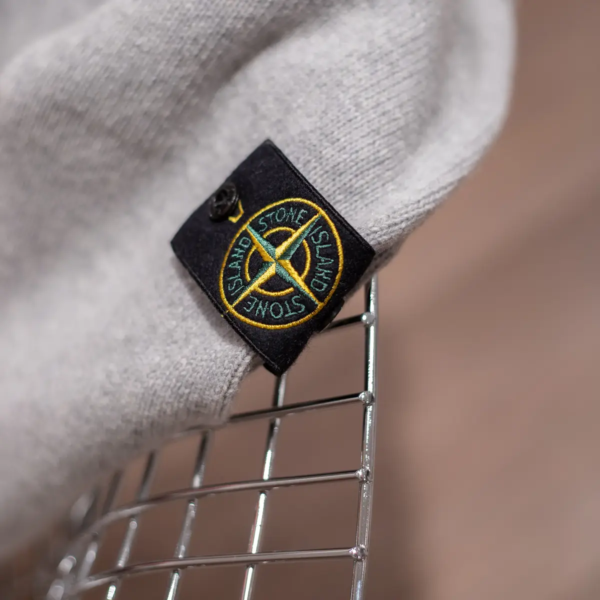 Grauer Pullover auf einem silbernen Stuhl mit Stone Island Badge im Fokus.
