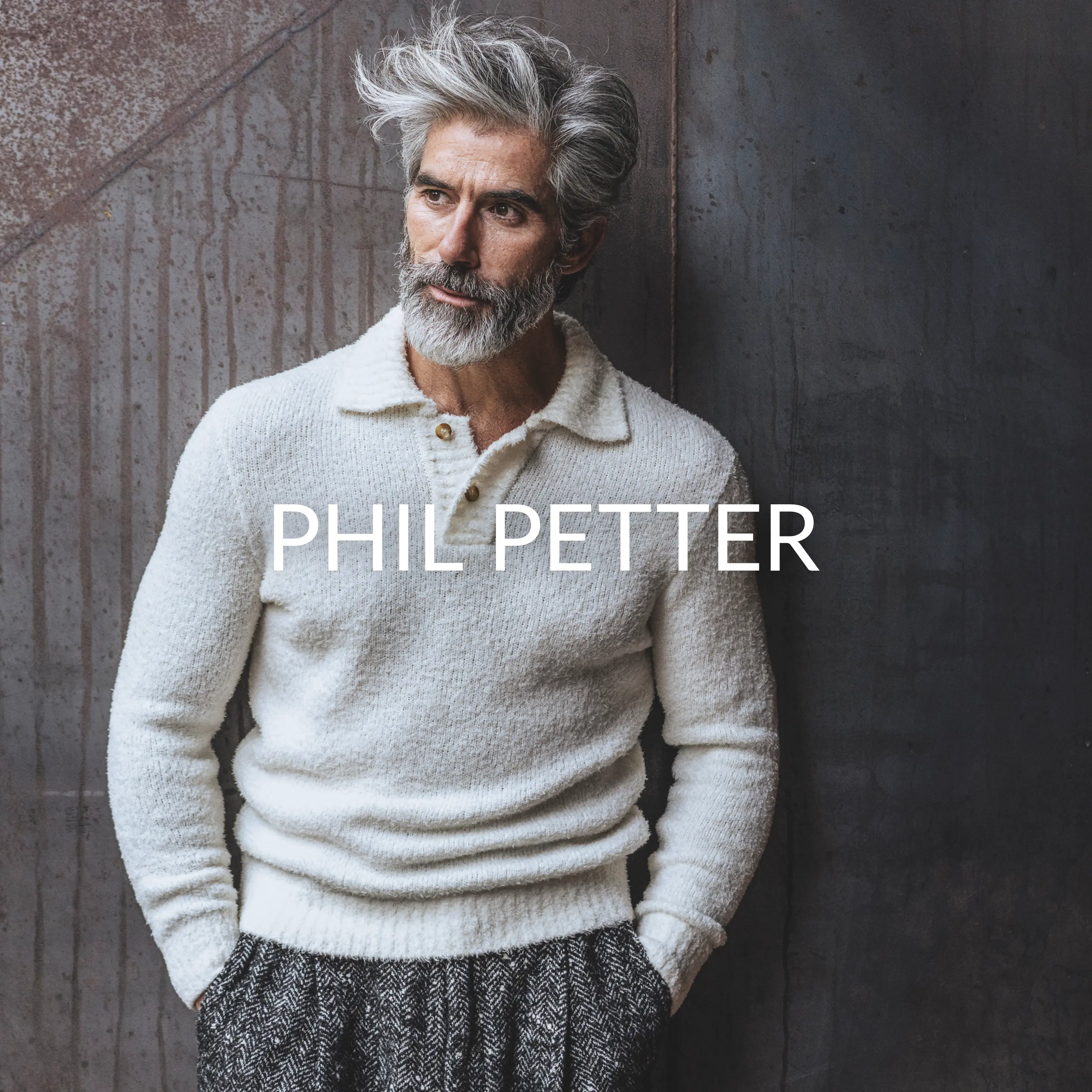 Mann in weißem Strickpullover mit Polokragen und grauer Stoffhose – Marke Phil Petter im Vordergrund.